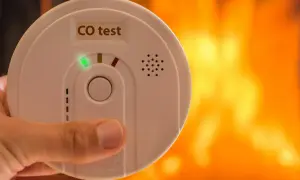 Détecteur de monoxyde de carbone tenu à la main, avec un feu de cheminée en arrière-plan. Où placer détecteur monoxyde de carbone ?