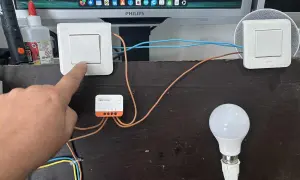Installation d'un interrupteur zigbee va et vient. Un doigt actionne un interrupteur connecté à un module Sonoff, pilotant une ampoule.
