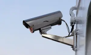 Caméra de surveillance extérieure, fixée sur un mur blanc. Le ciel bleu clair est visible derrière. On dirait qu'il y a un probleme camera de surveillance pas d'image.