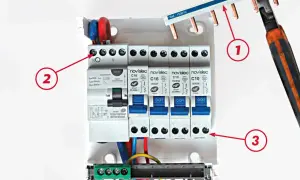 Un tableau électrique avec un interrupteur différentiel et des disjoncteurs. Le câblage est en cours, avec des fils rouges, bleus et jaunes.
