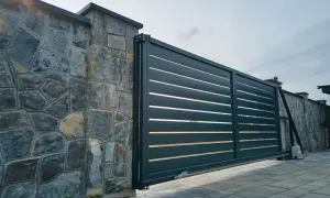 Portail coulissant moderne, presque entièrement ouvert à 120 degrés, longeant un mur de pierres brutes.
