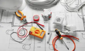 Outils d'électricien et composants sur un plan, pour un devis électricité exemple. Pince, multimètre, prise, ampoules, disjoncteur, ruban adhésif.