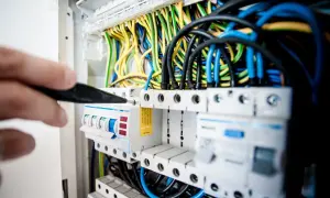 Main électrique avec fils colorés. Un tournevis ajuste un disjoncteur, peut-être un délesteur électrique, dans un tableau.