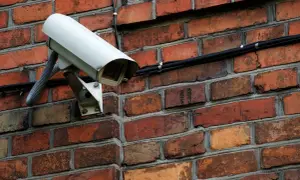 Caméra de surveillance blanche fixée sur un mur de briques. Comment reconnaître une caméra factice ? Cherchez l'absence de câbles ou de voyants lumineux.