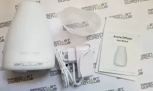 Un diffuseur d'arômes blanc, son adaptateur et son manuel. Un objet connecté pour une ambiance olfactive personnalisée.