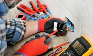 Un électricien utilise des outils pour installer une prise. On voit des fils, un tournevis, un multimètre et d'autres outils pour électricien.