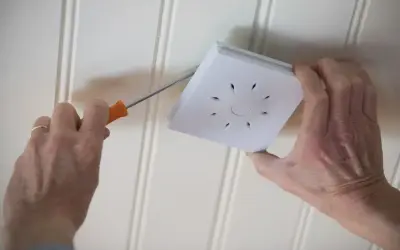 Main tenant répare un détecteur de fumée qui se déclenche sans raison. Il utilise un tournevis pour le démonter.