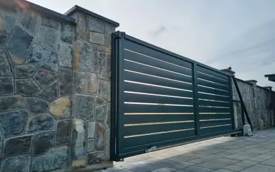 Portail coulissant moderne, presque entièrement ouvert à 120 degrés, longeant un mur de pierres brutes.