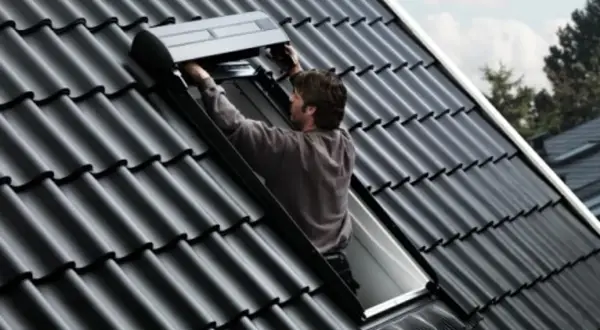 Un couvreur installe un volet roulant sur un toit en tuiles noires, un modèle velux 3uc b01 eu.