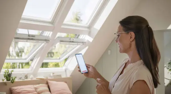 Une femme utilise son smartphone pour piloter des fenêtres de toit Velux.