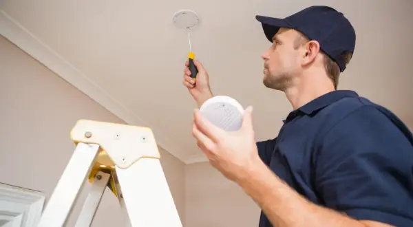 Un technicien installe des alarmes incendie au plafond, assurant la sécurité de votre domicile.