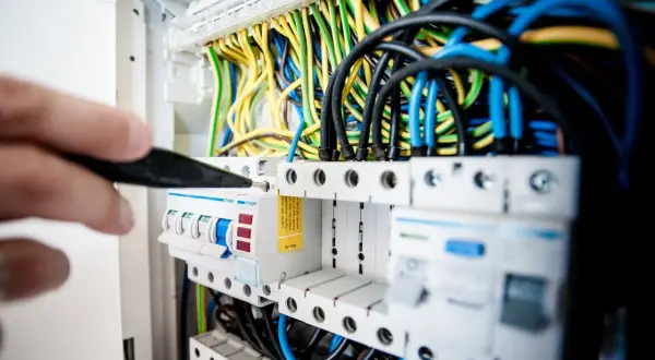 Main électrique avec fils colorés. Un tournevis ajuste un disjoncteur, peut-être un délesteur électrique, dans un tableau.