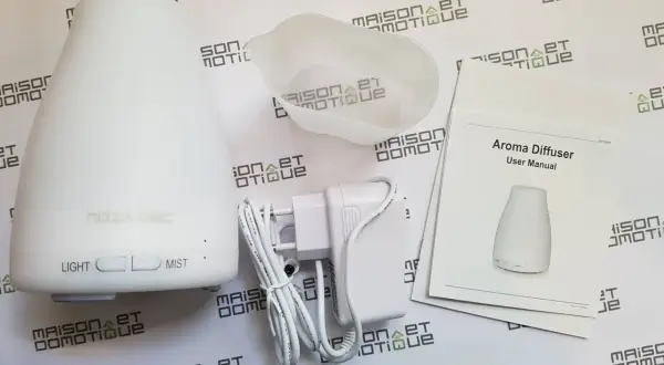 Un diffuseur d'arômes blanc, son adaptateur et son manuel. Un objet connecté pour une ambiance olfactive personnalisée.