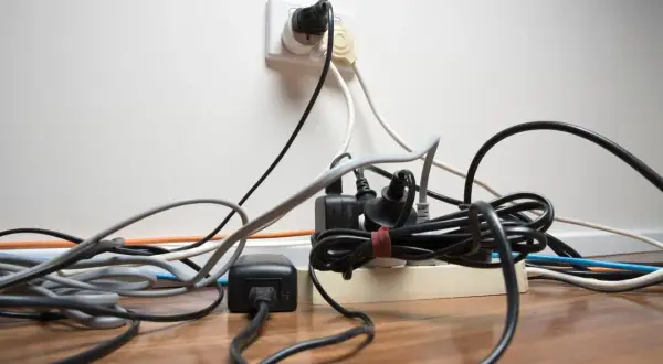 Un enchevêtrement de fils électriques branchés sur une multiprise et une prise murale. Un vrai défi pour faire de l'électricité soi-même sans s'emmêler !