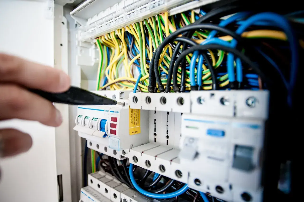 Main électrique avec fils colorés. Un tournevis ajuste un disjoncteur, peut-être un délesteur électrique, dans un tableau.