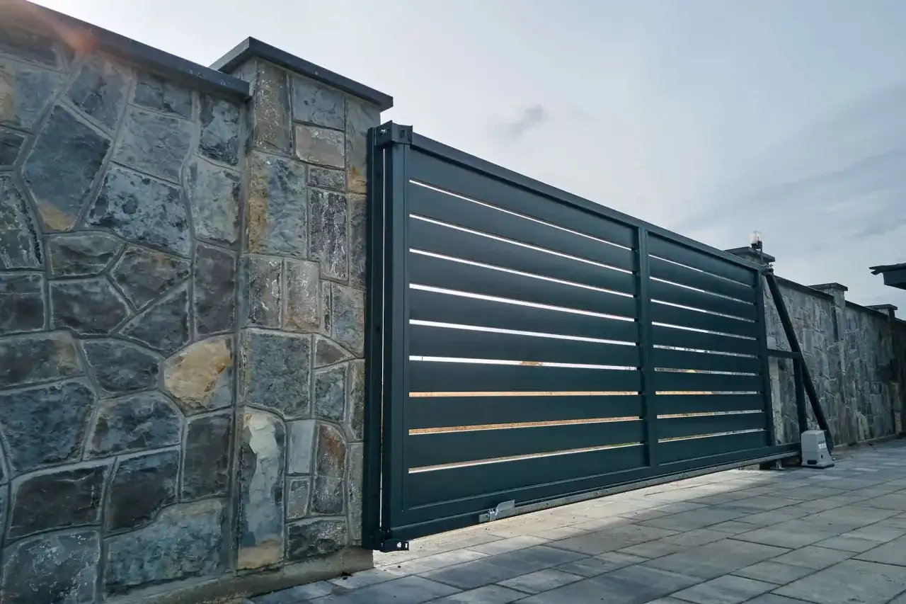 Portail coulissant moderne, presque entièrement ouvert à 120 degrés, longeant un mur de pierres brutes.