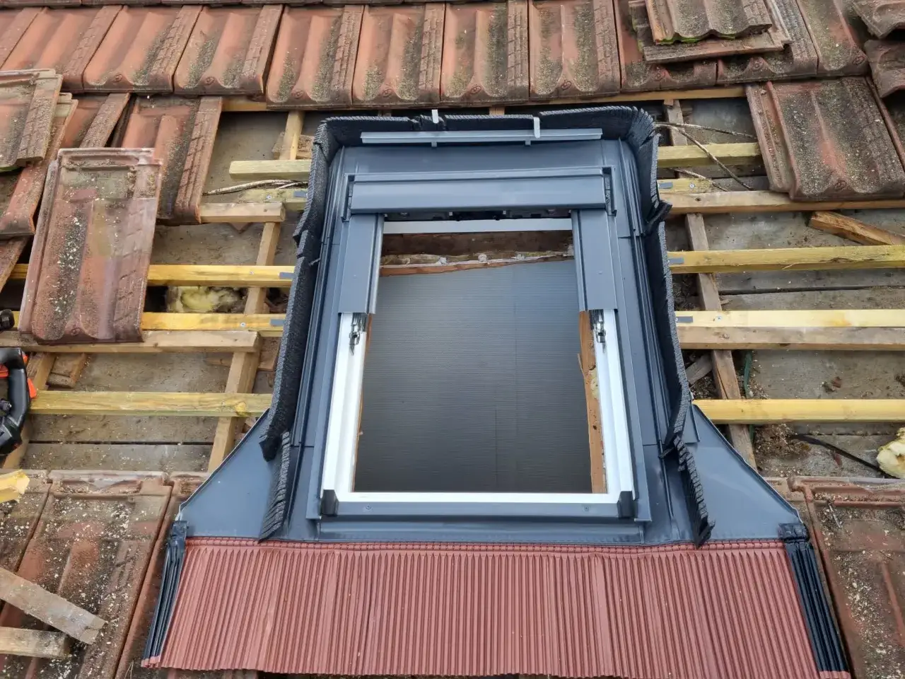 Installation d'une fenêtre de toit velux 3uc b01 eu sur un toit en tuiles rouges, en cours de rénovation.