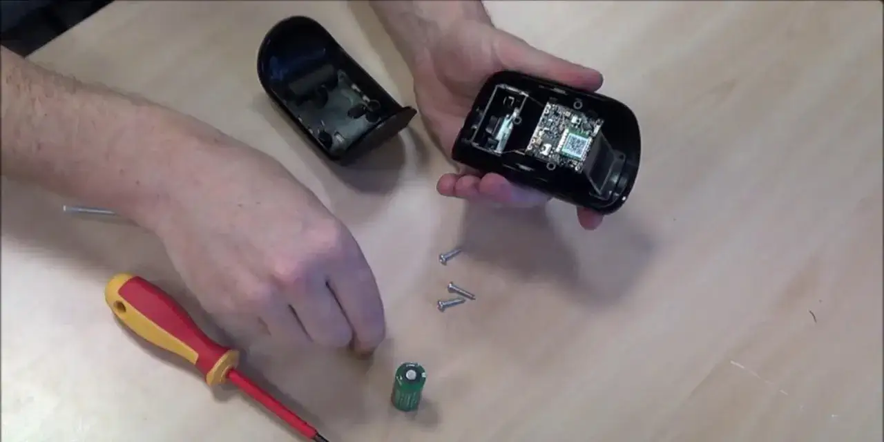 D&eacute;montage d'une alarme filaire pour v&eacute;rifier la dur&eacute;e de vie batterie. Une pile et des vis sont visibles.
